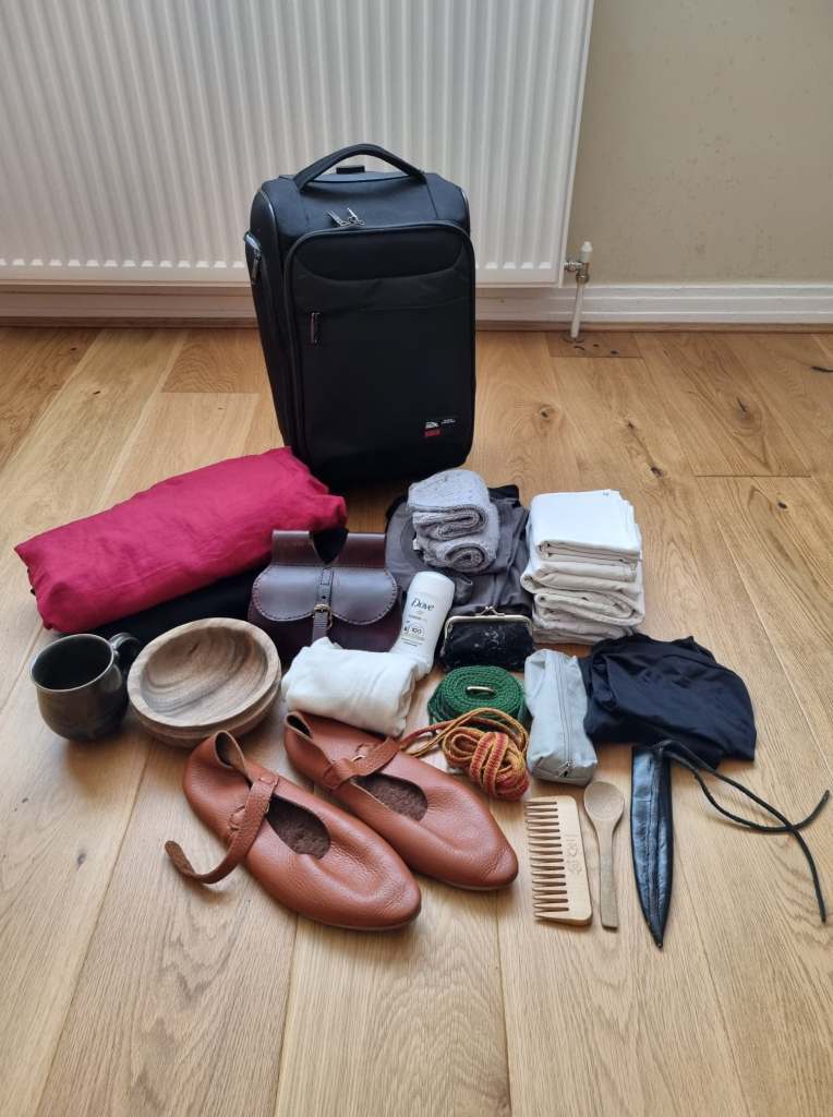Photograph of a small black cabin bag with clothing, shoes, and tableware laid out on the floor in front of it.
